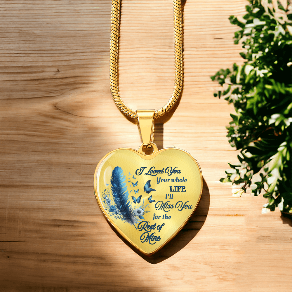 Gold heart-shaped pendant with blue feather and engraved sentimental text on a gold chain.