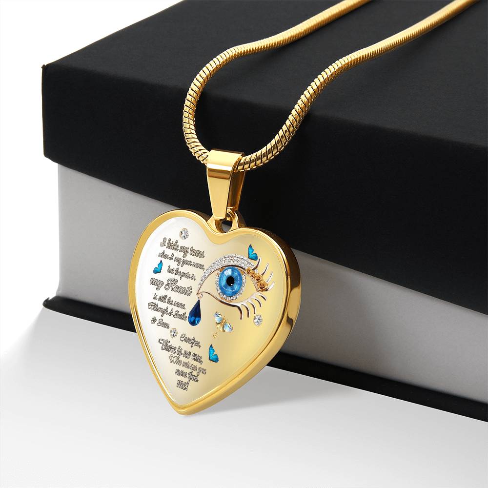 Gold heart-shaped necklace pendant with blue eye and tear drop design, engraved script, on snake chain.