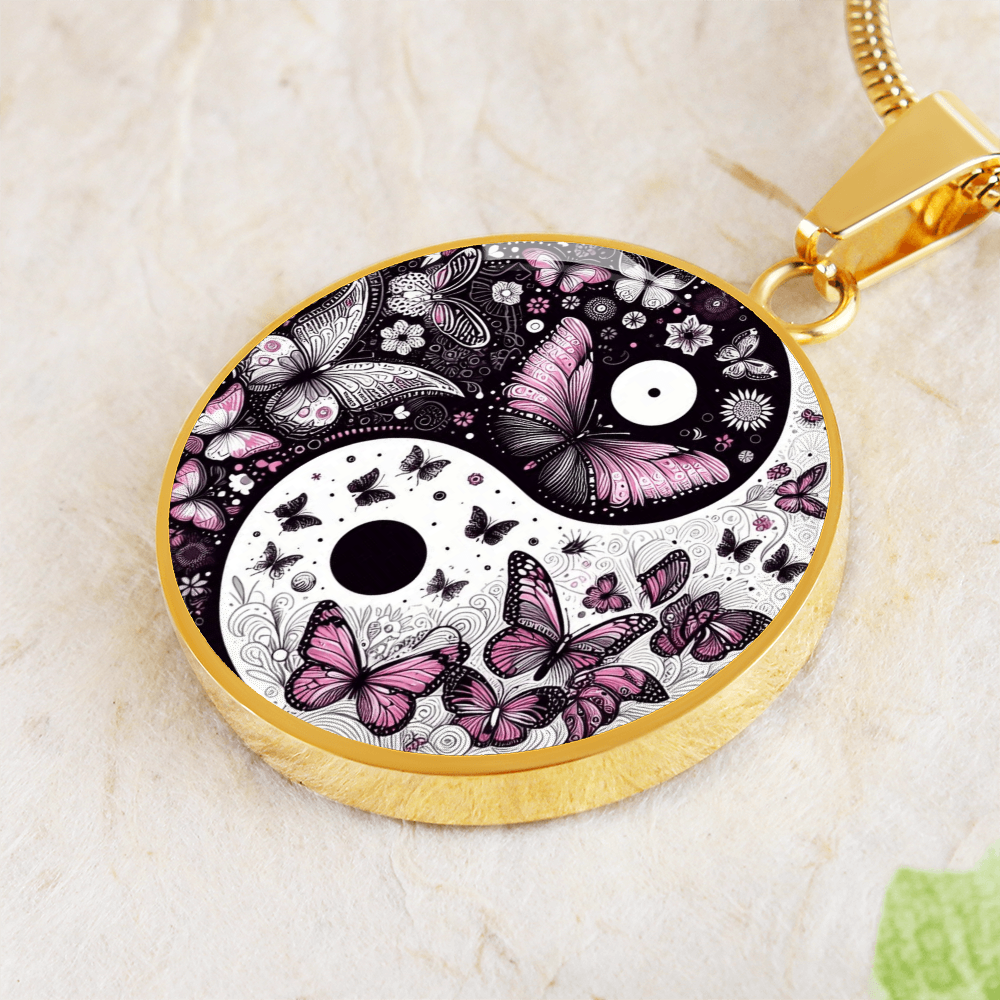 Close-up of a gold yin and yang pendant necklace featuring pink and black butterflies and flowers.