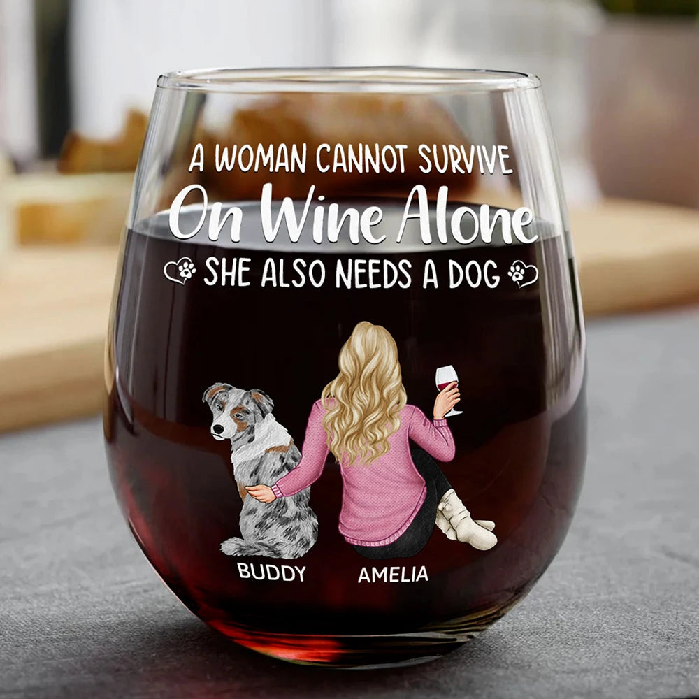 A large glass of red wine with a white design depicting a woman, "Amelia," with blonde hair and a pink sweater, sitting next to a dog, "Buddy," under the text "A WOMAN CANNOT SURVIVE On Wine Alone SHE ALSO NEEDS A DOG".