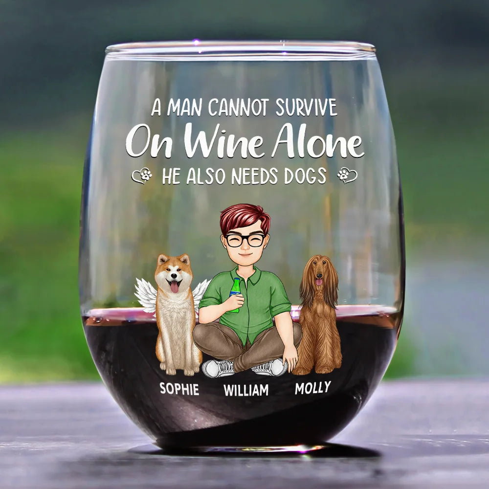 A glass of red wine with a cartoon illustration of a man and two dogs on it. The man is wearing a green shirt and brown pants. One dog is light brown with white angel wings, and the other is dark brown with long hair. The names "Sophie," "William," and "Molly" are written below each character. The text above the illustration reads "A man cannot survive on wine alone, he also needs dogs."