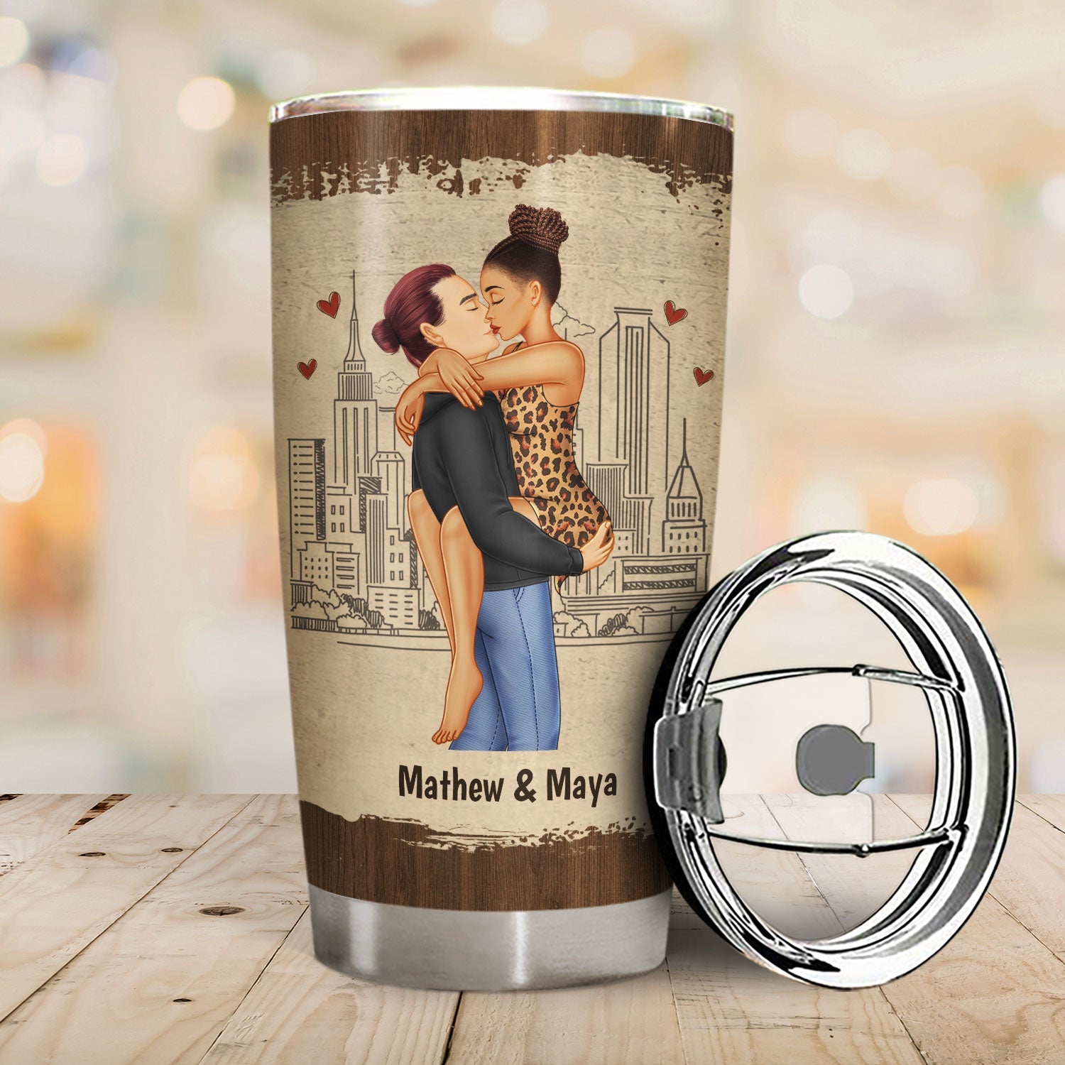 Tumbler with illustration of a couple embracing against a cityscape background, with lid beside it.