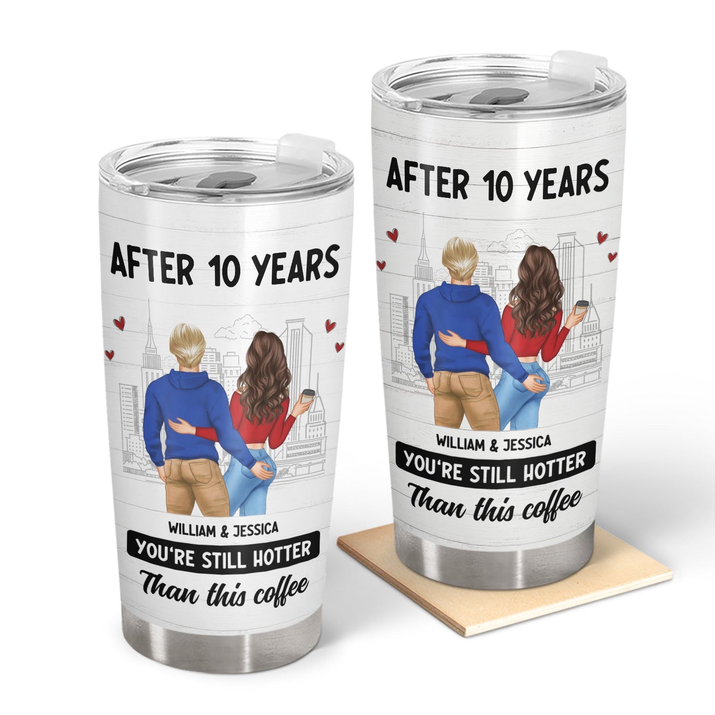 Two white tumblers with a cartoon couple illustration. The man wears a blue sweater and khaki pants. The woman wears a red sweater and blue jeans. They are embracing and holding hands. In the background, there is a cityscape with hearts floating around them. Above the couple are the words, "AFTER 10 YEARS," and below them, "WILLIAM & JESSICA," and "YOU'RE STILL HOTTER Than this coffee." One tumbler is standing on a wooden coaster.
