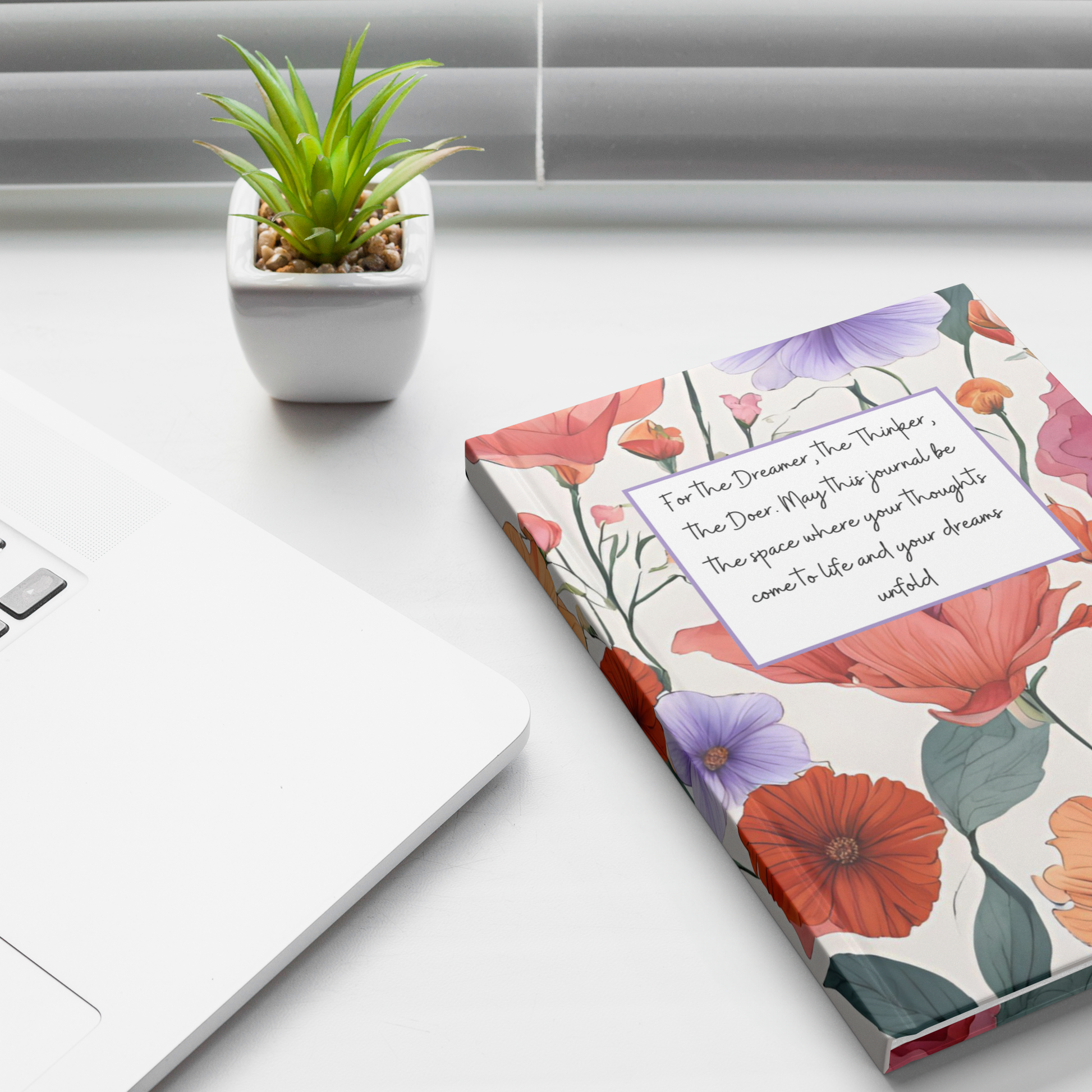 Floral notebook with red, purple, and orange flowers and a white label reading inspirational quote on a white desk next to a .
