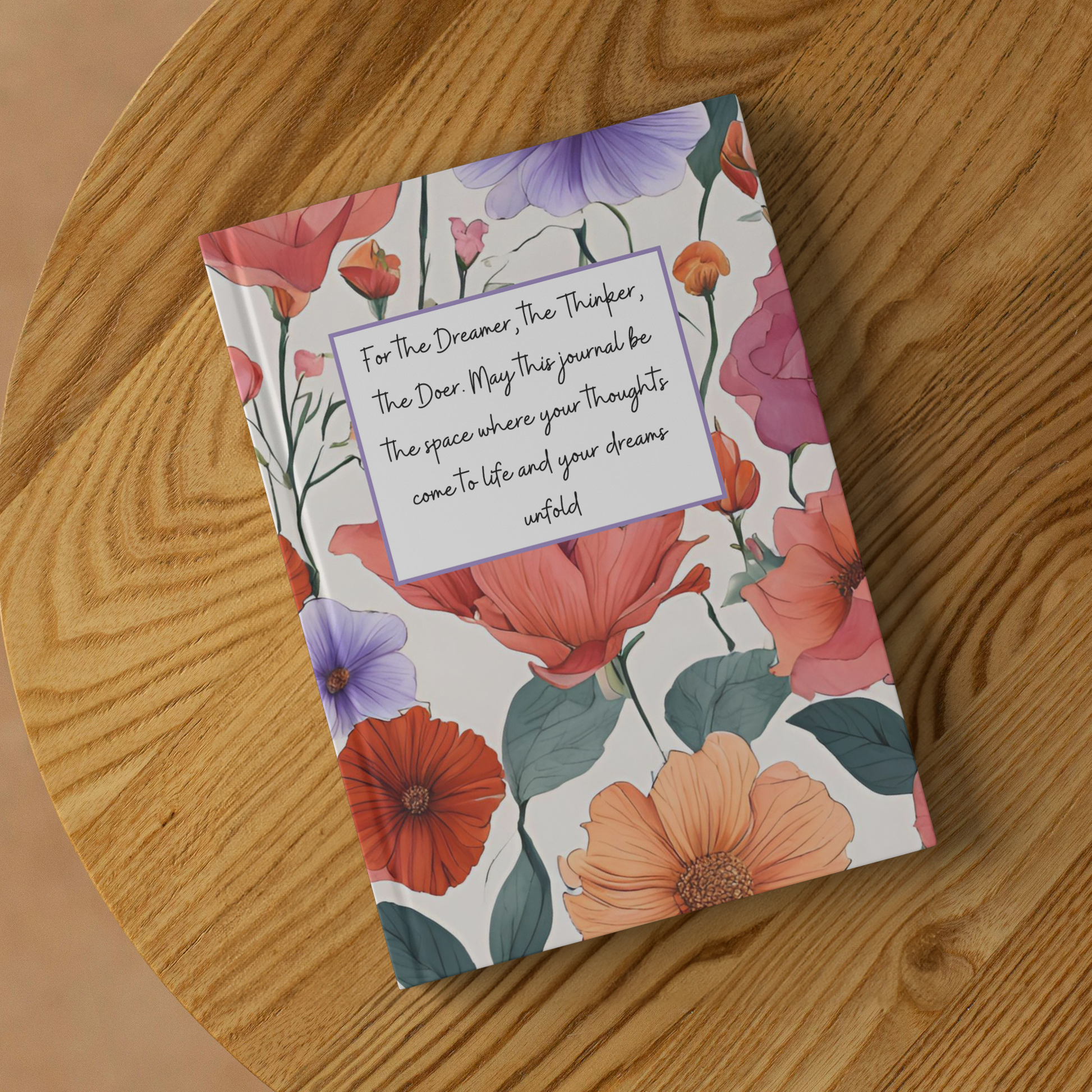 Notebook with colorful floral cover and motivational quote on wooden surface.