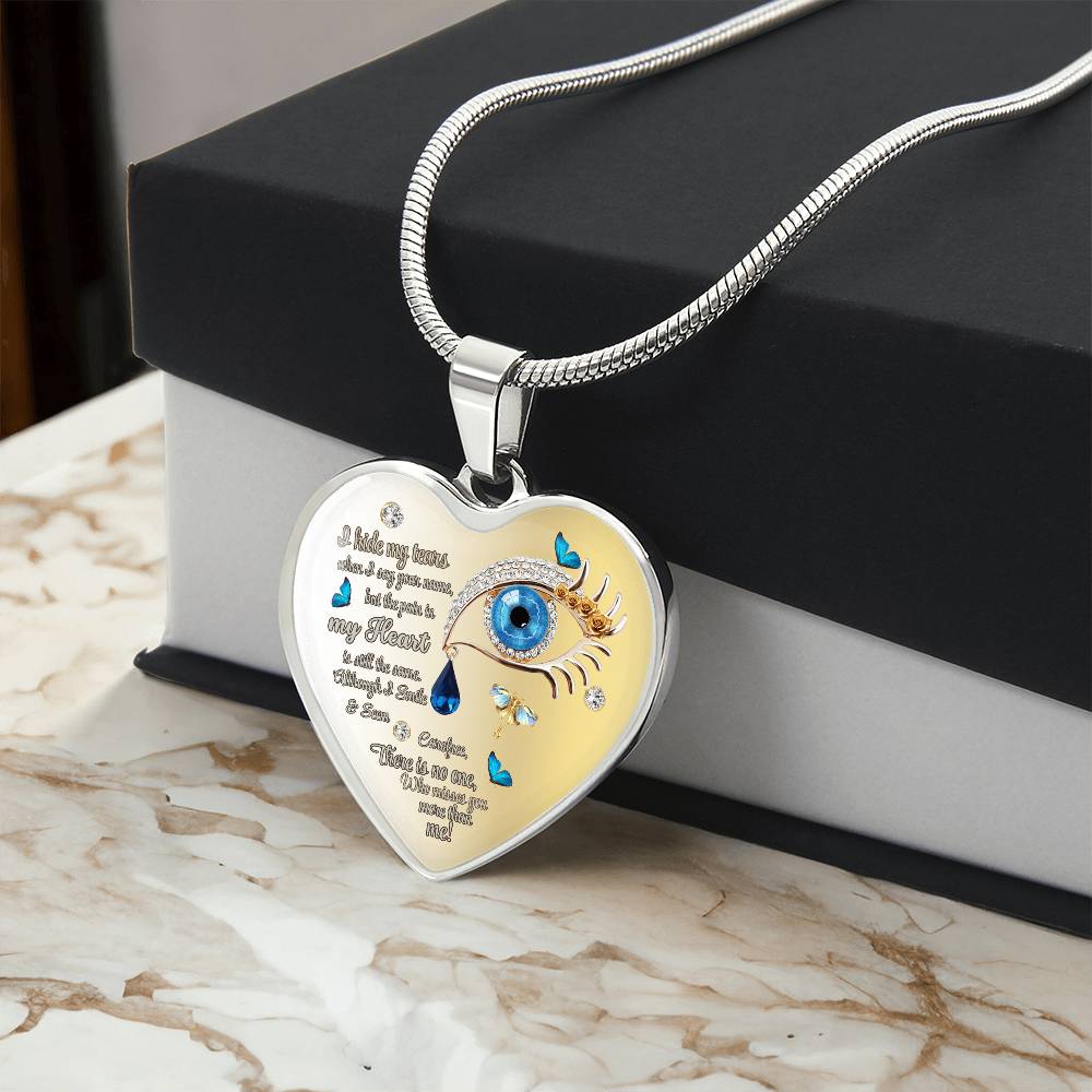Silver heart-shaped necklace pendant with blue eye, engraved tears, and poetic text on a snake chain.