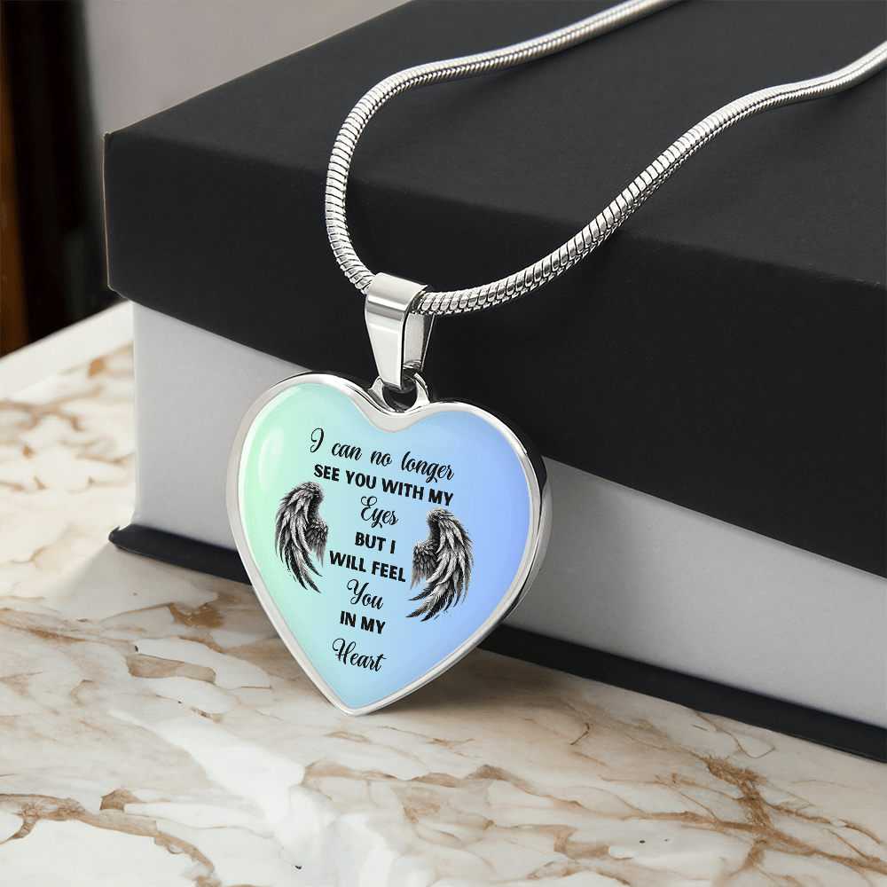 Heart-shaped pendant necklace with angel wings design and inspirational quote on a marble surface next to a black jewelry box.