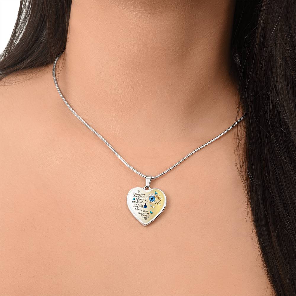 Silver heart-shaped pendant necklace with graphic design and small blue gem on woman’s neck.