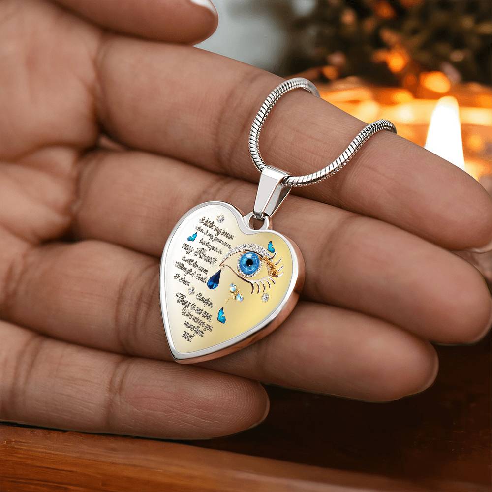 Silver heart-shaped necklace pendant with engraved text and blue eye charm with tear drops.