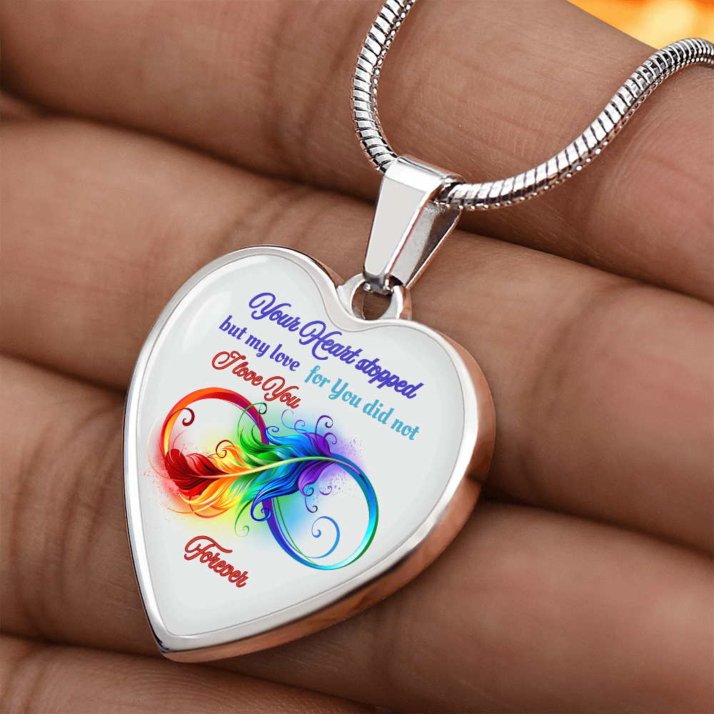 Silver heart-shaped pendant with colorful feather design and blue and red script text on snake chain.