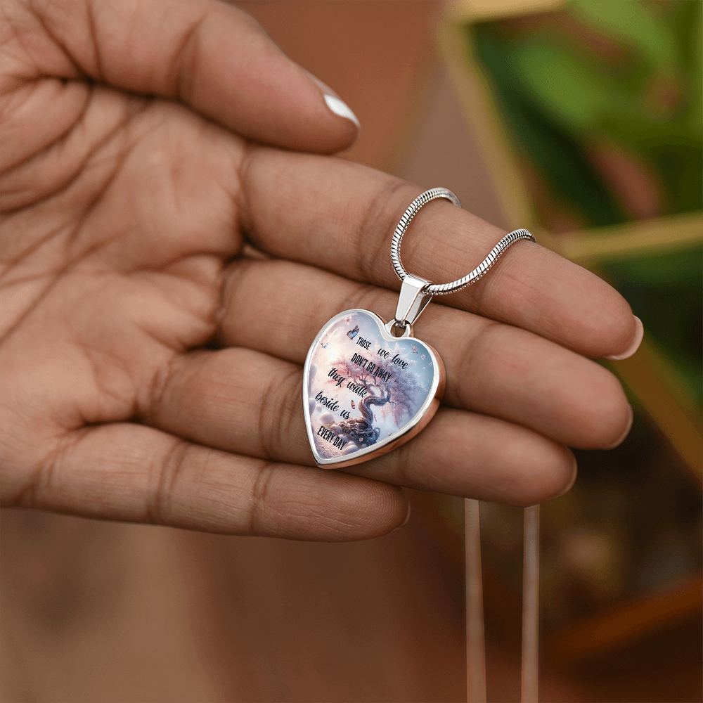 Silver heart-shaped necklace pendant with tree and sentimental inscription, held in hand.