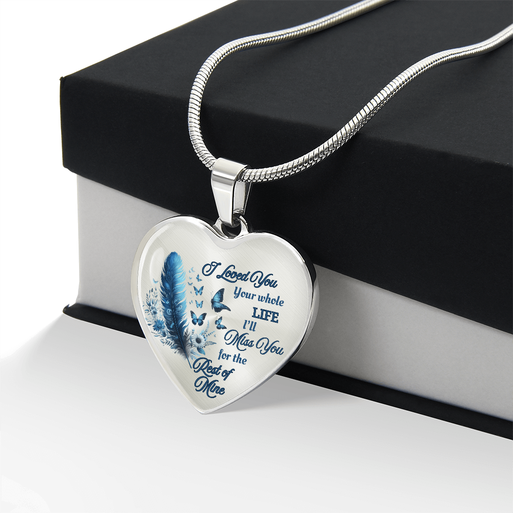 Silver heart-shaped pendant necklace with blue feather and engraved sentimental message on a black and white box.