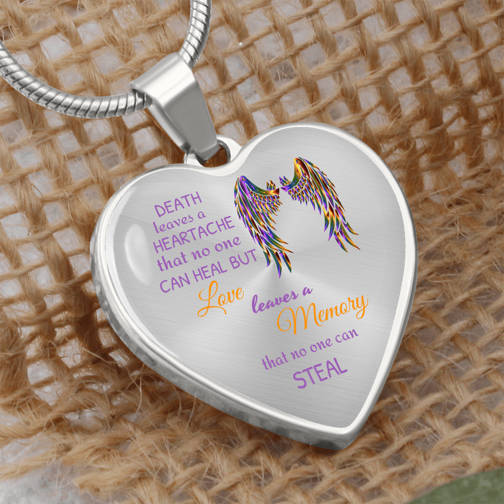 Close-up of a heart-shaped pendant necklace with angel wings and text on a textured beige surface.