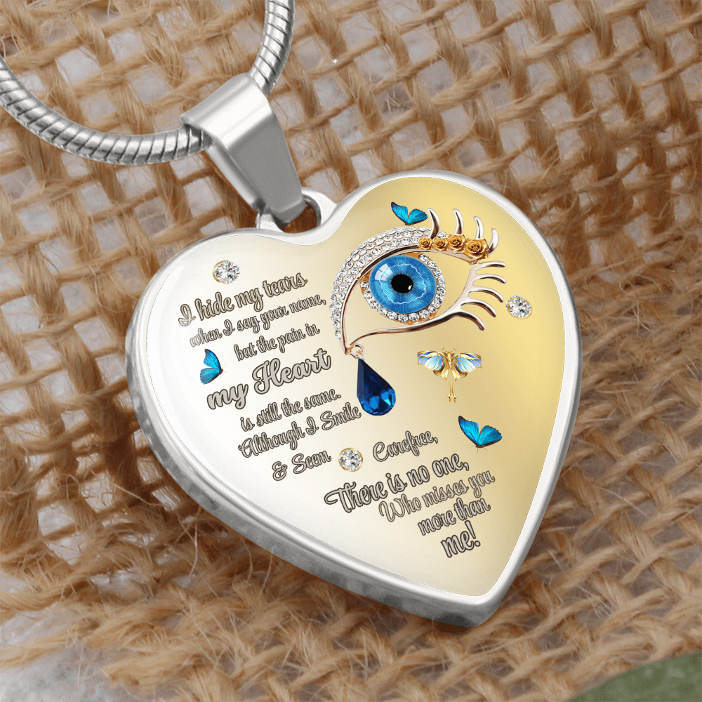 Silver heart-shaped necklace pendant with blue eye, tear drop, and engraved poetic text on woven background.