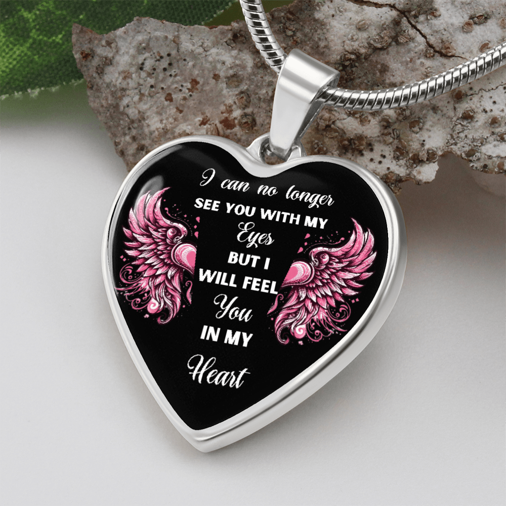 Heart-shaped silver pendant with black background, pink angel wings, and white memorial inscription.