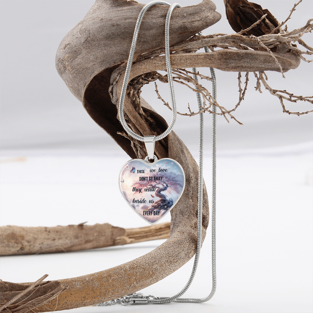 Silver heart-shaped necklace pendant with engraved sentimental message, hanging on thin silver chain over driftwood display.