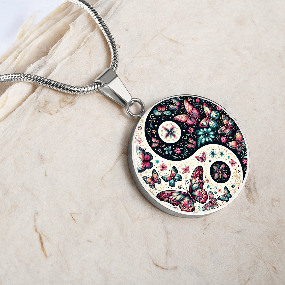 Close-up of a silver yin-yang pendant necklace with a colorful butterfly and flower design on a textured, off-white surface.