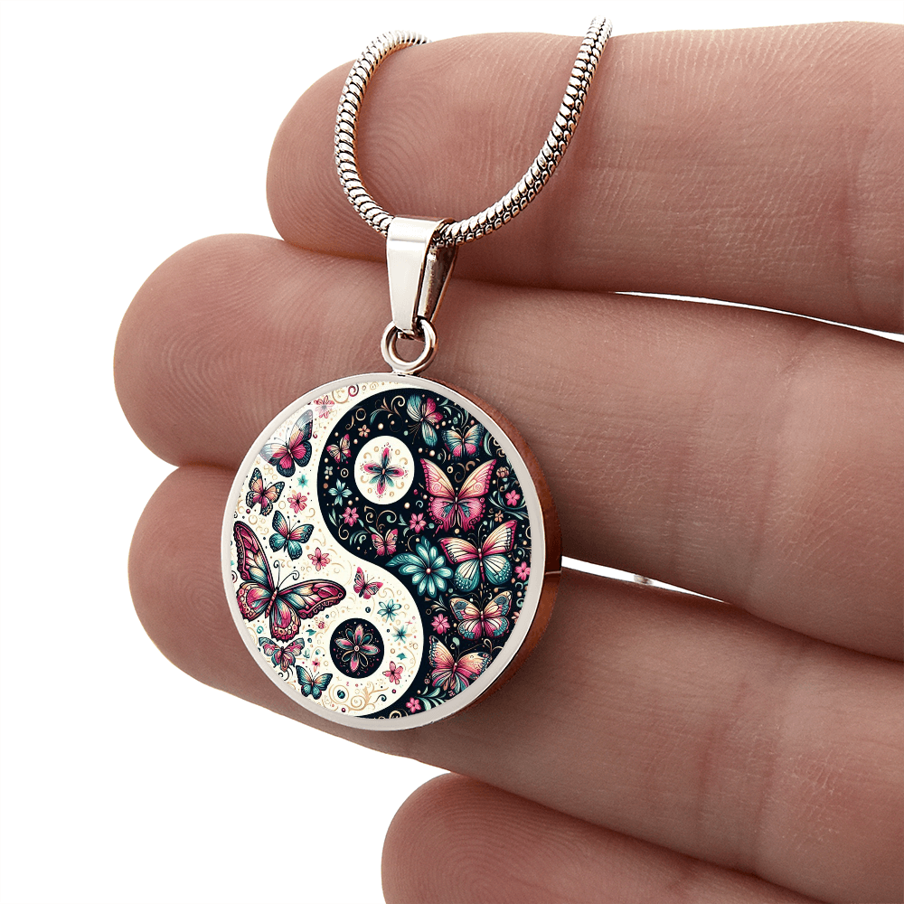 Close-up of a hand holding a yin-yang pendant with a butterfly and flower design, attached to a silver snake chain.