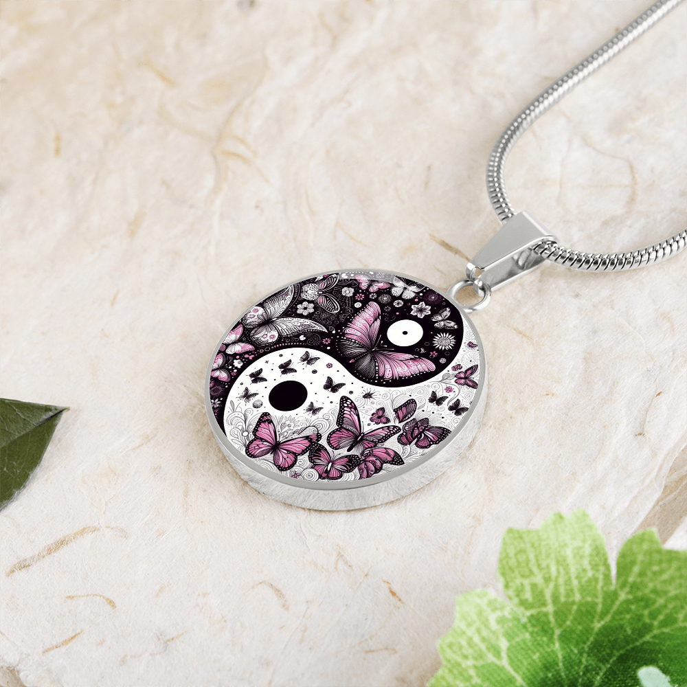 Yin-yang butterfly pendant necklace on textured surface with greenery.
