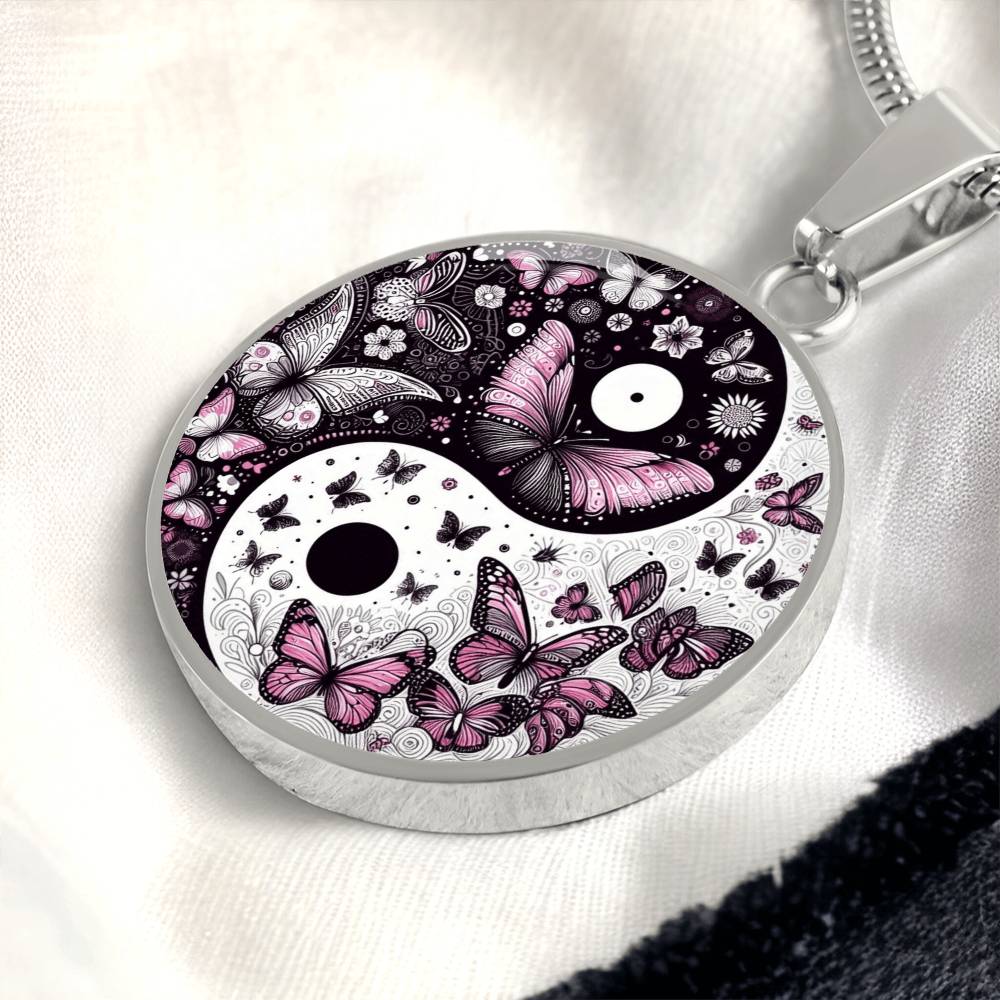Close-up of a silver pendant necklace featuring a yin yang design with black and pink butterflies and flowers.