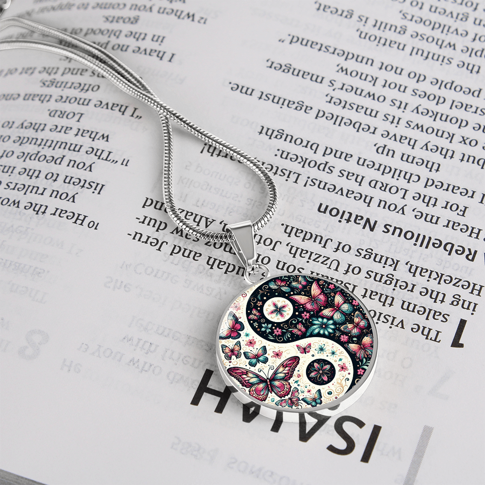 A necklace featuring a yin and yang design with butterflies and flowers, resting on an open Bible.