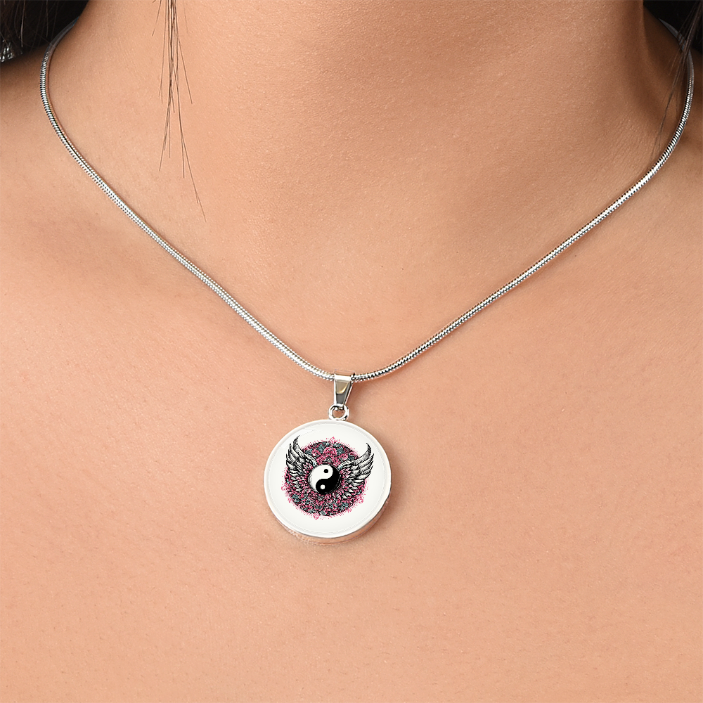 Silver necklace with circular pendant featuring pink angel wings forming a yin yang symbol.