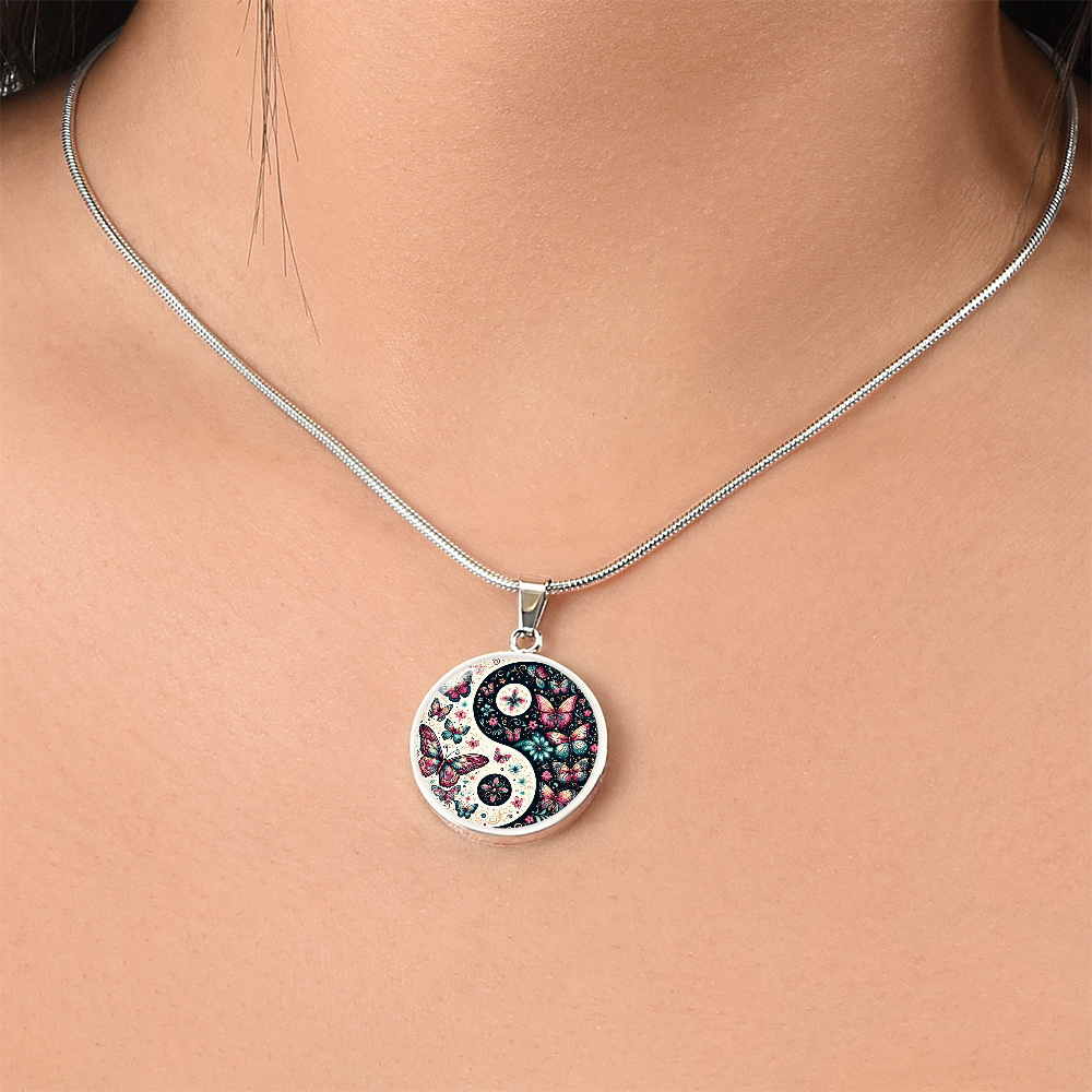 Close-up of a silver snake chain necklace with a circular pendant featuring a yin-yang symbol filled with butterfly and floral designs.
