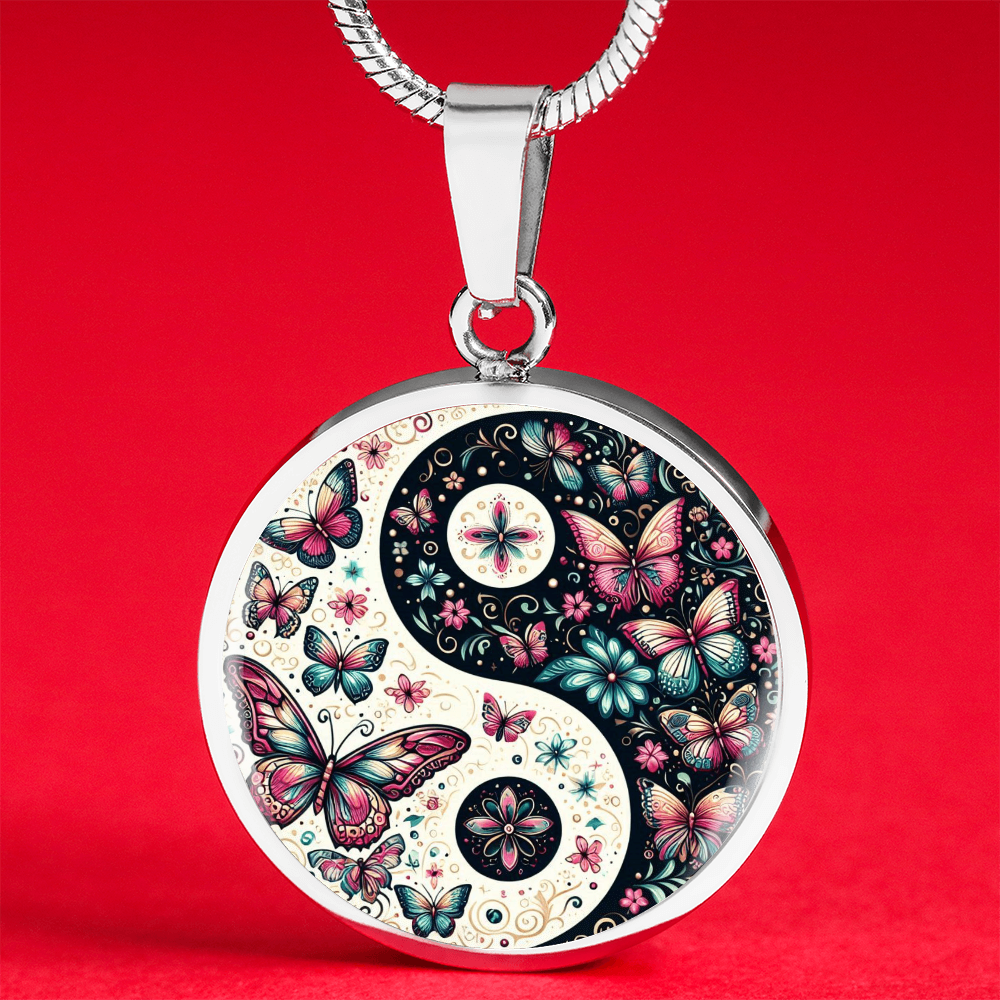 Close-up of a round silver pendant necklace with a yin and yang design filled with colorful butterflies and flowers, on a red background.