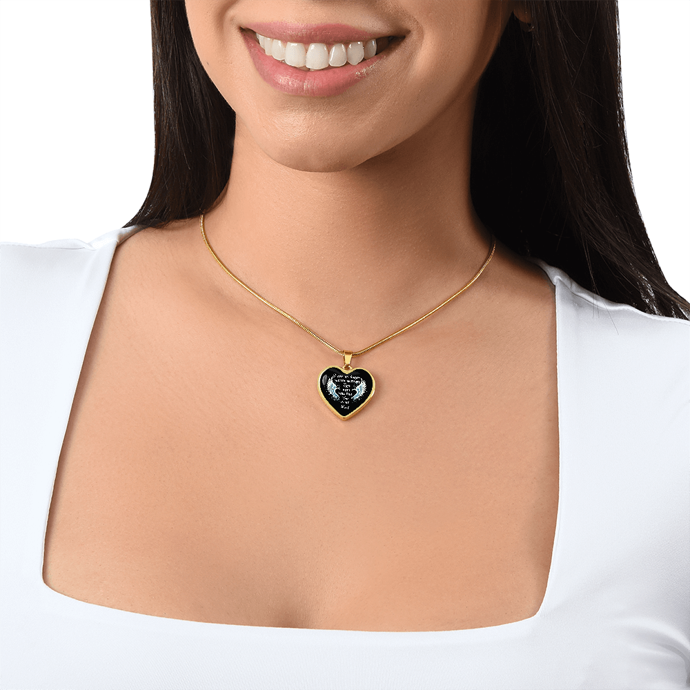 A woman wears a gold heart-shaped necklace with a black background and white text. She wears a white shirt and smiles.