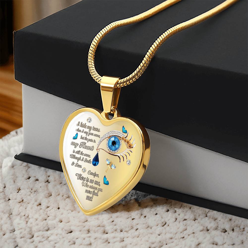 Gold heart-shaped necklace with engraved tear drop text and blue eye detail on a chain.