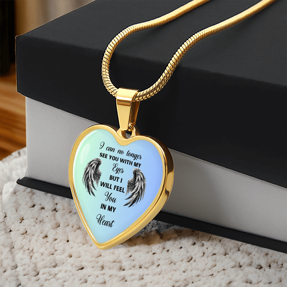 Gold heart-shaped pendant necklace with angel wings and engraved memorial text on light blue background.