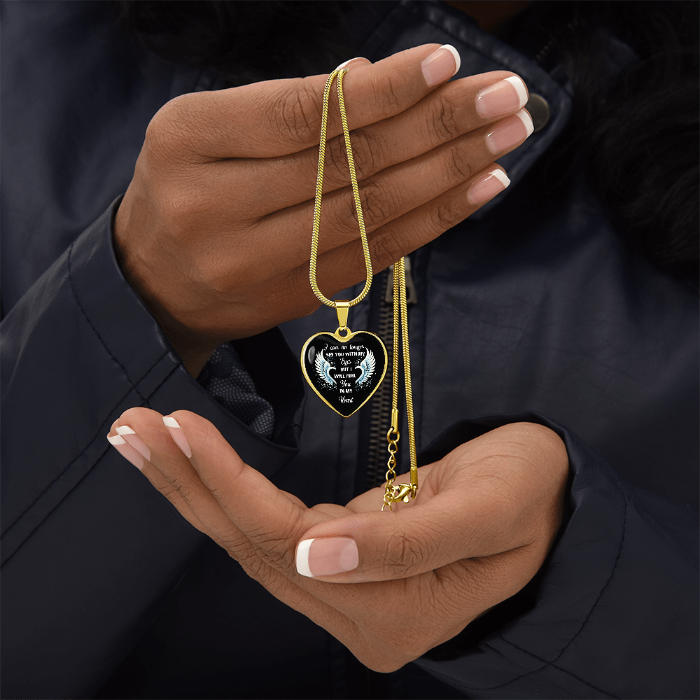 A person wearing a black jacket is holding up a heart-shaped pendant necklace with a gold chain.