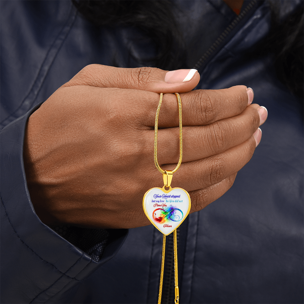Gold heart-shaped pendant necklace with colorful infinity and text engraving held in hand.