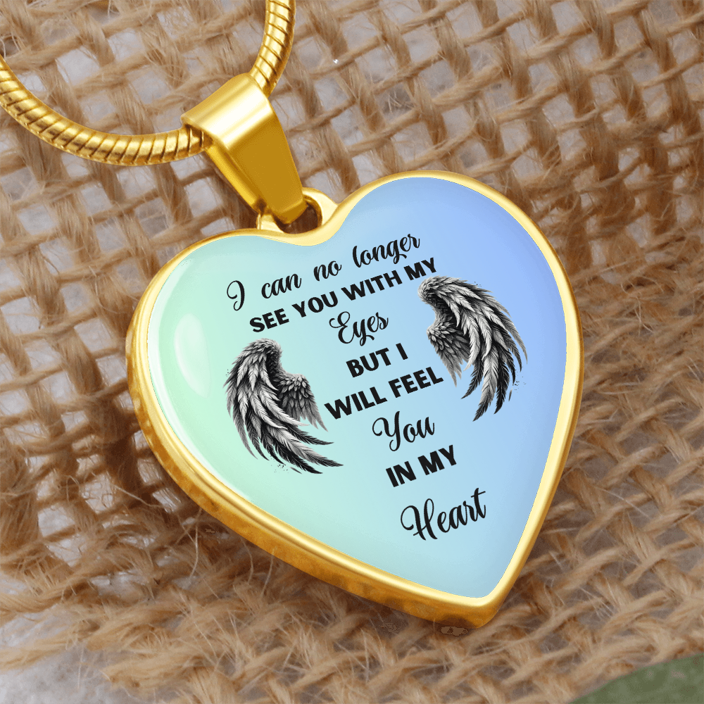 Close-up of a heart-shaped pendant with a gold chain. The pendant has angel wings and a sentimental message.