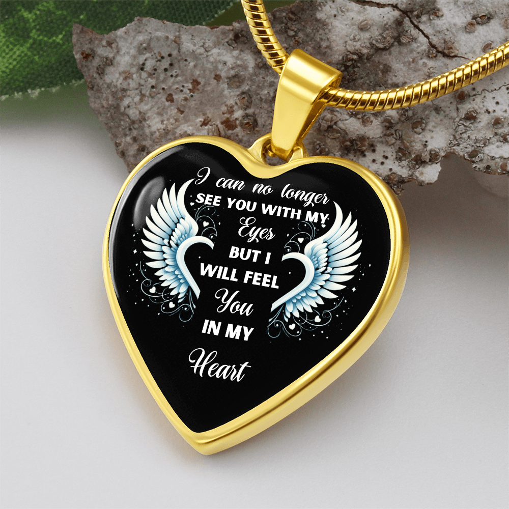 Close-up of a heart-shaped gold-rimmed pendant with a black background featuring a white quote: "I can no longer see you with my eyes but I will feel you in my heart" with two white angel wings on each side.