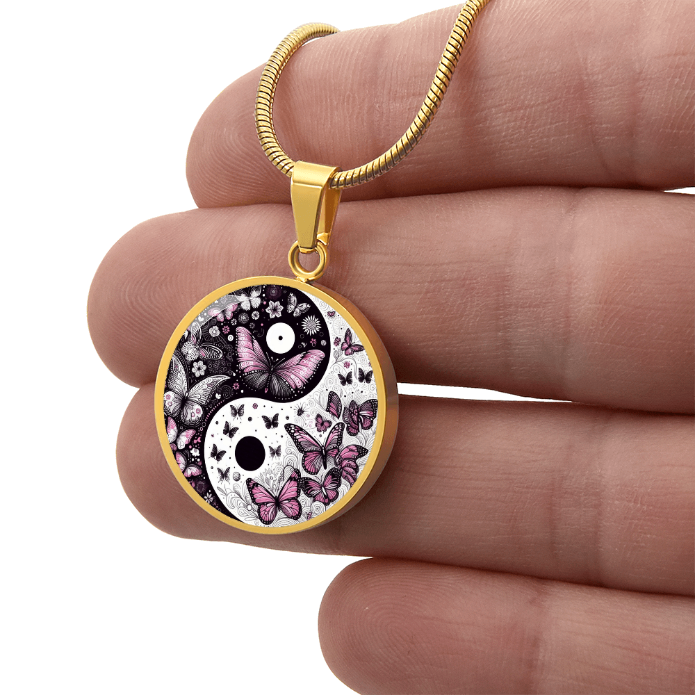 Close-up of a gold necklace with a yin-yang pendant featuring a butterfly design, held in a hand.