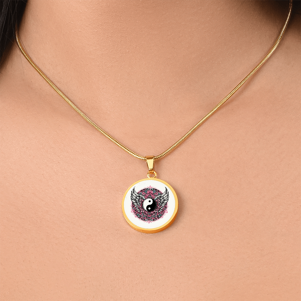 Gold round pendant necklace with yin yang symbol and detailed angel wings on white background.