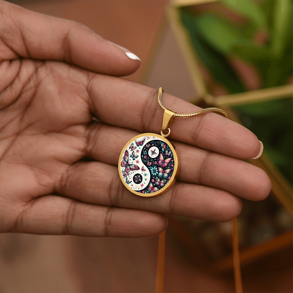 Gold circle necklace pendant with pink and black butterfly yin yang design held in hand.