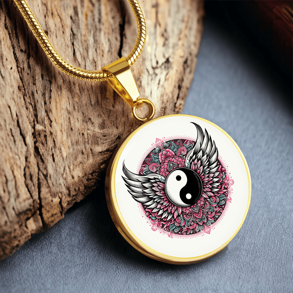 Gold necklace with round pendant featuring yin yang symbol and detailed angel wings over pink floral background.