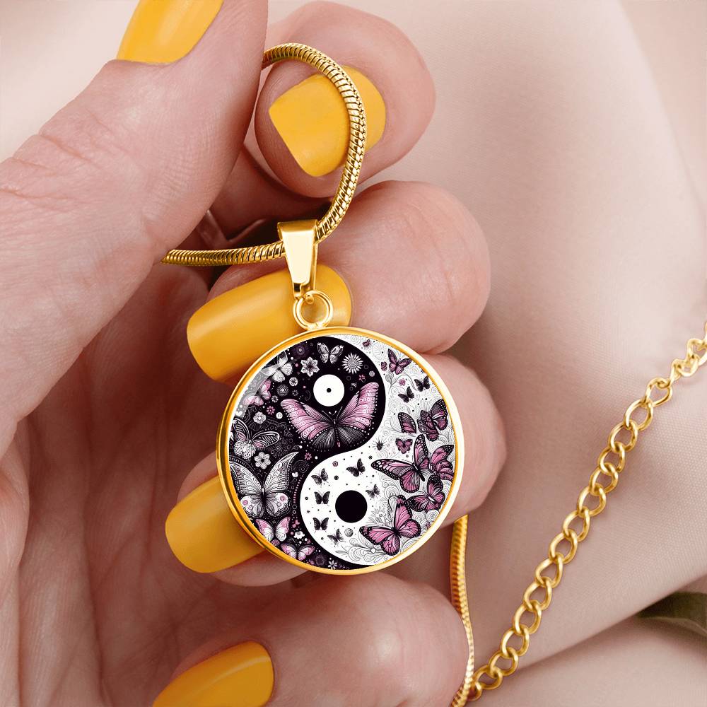 Close-up of hand holding a gold yin-yang necklace with butterfly design. Nails are yellow.