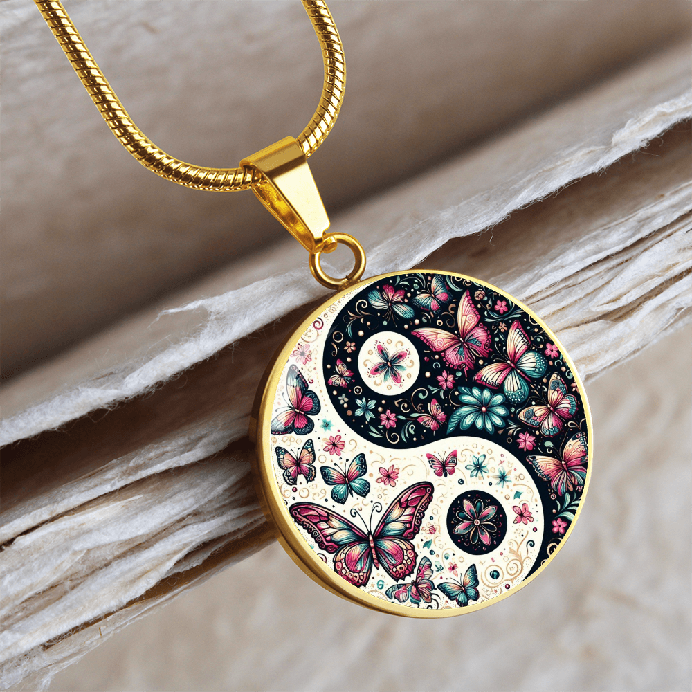 Gold circular yin yang pendant adorned with pink and blue butterfly designs on a gold snake chain necklace.