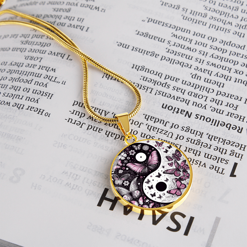 Gold necklace with a butterfly-themed yin-yang pendant on a Bible page.