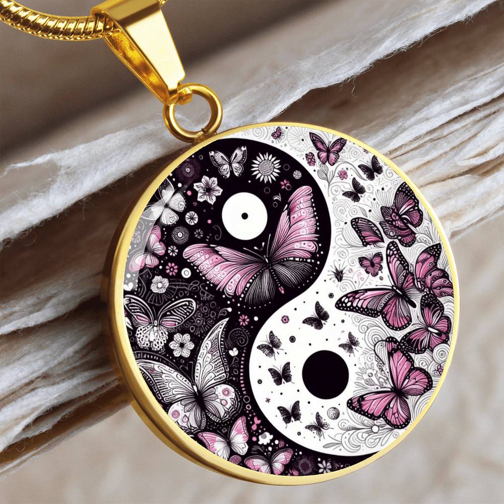 Close-up of a gold pendant with a yin and yang symbol filled with pink and white butterflies, hanging from a gold chain.