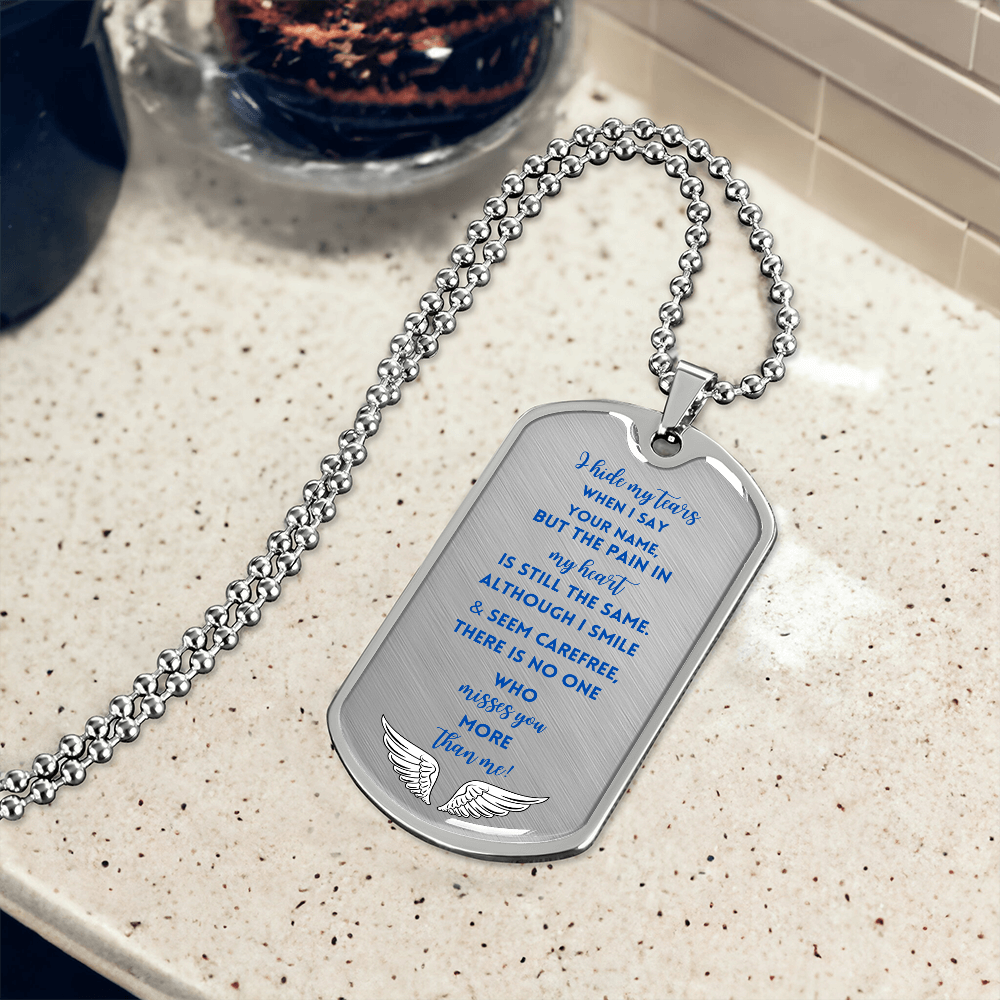 Silver military dog tag necklace with engraved sentimental prayer text and praying hands symbol on a speckled beige surface.