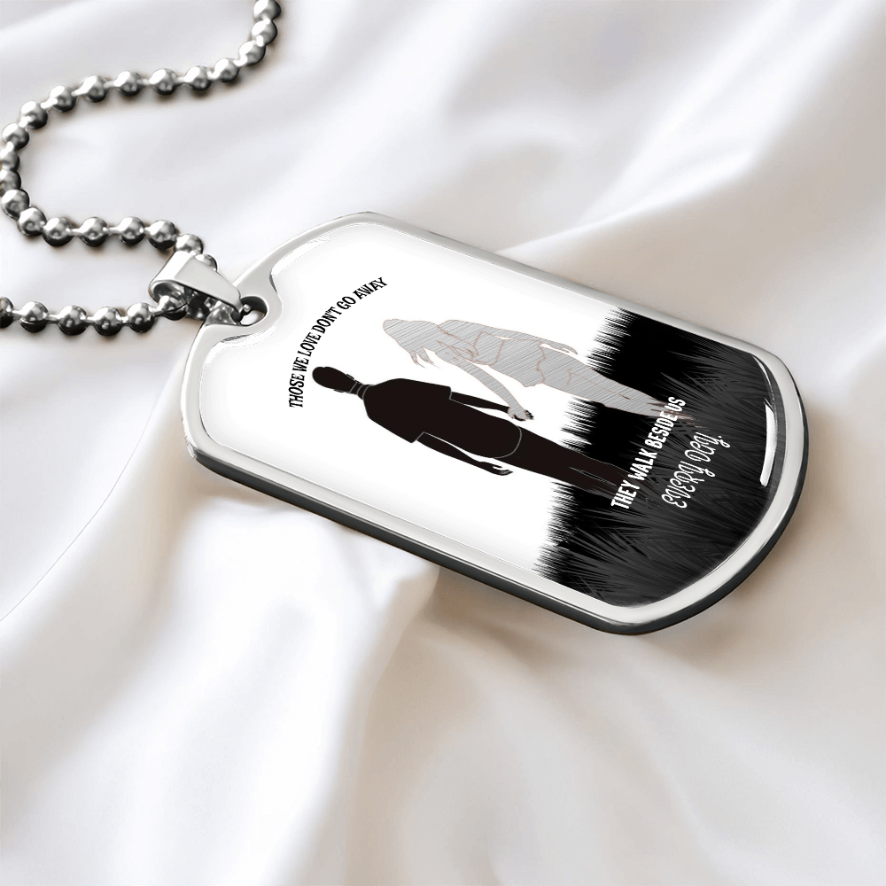 Silver military dog tag necklace with engraved soldier silhouettes and remembrance text on satin background.