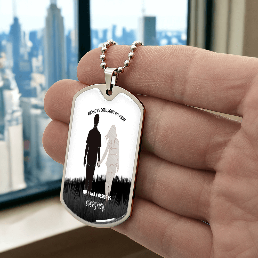 Silver metal military dog tag necklace with engraved silhouette and memorial message held in hand.