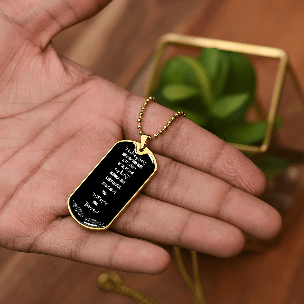 Black military tag necklace with gold trim and ball chain, engraved sentimental message, held in hand.