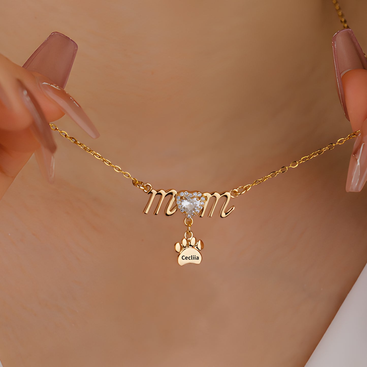 Gold necklace with "mom" script, heart-shaped crystal, and engraved paw pendant.