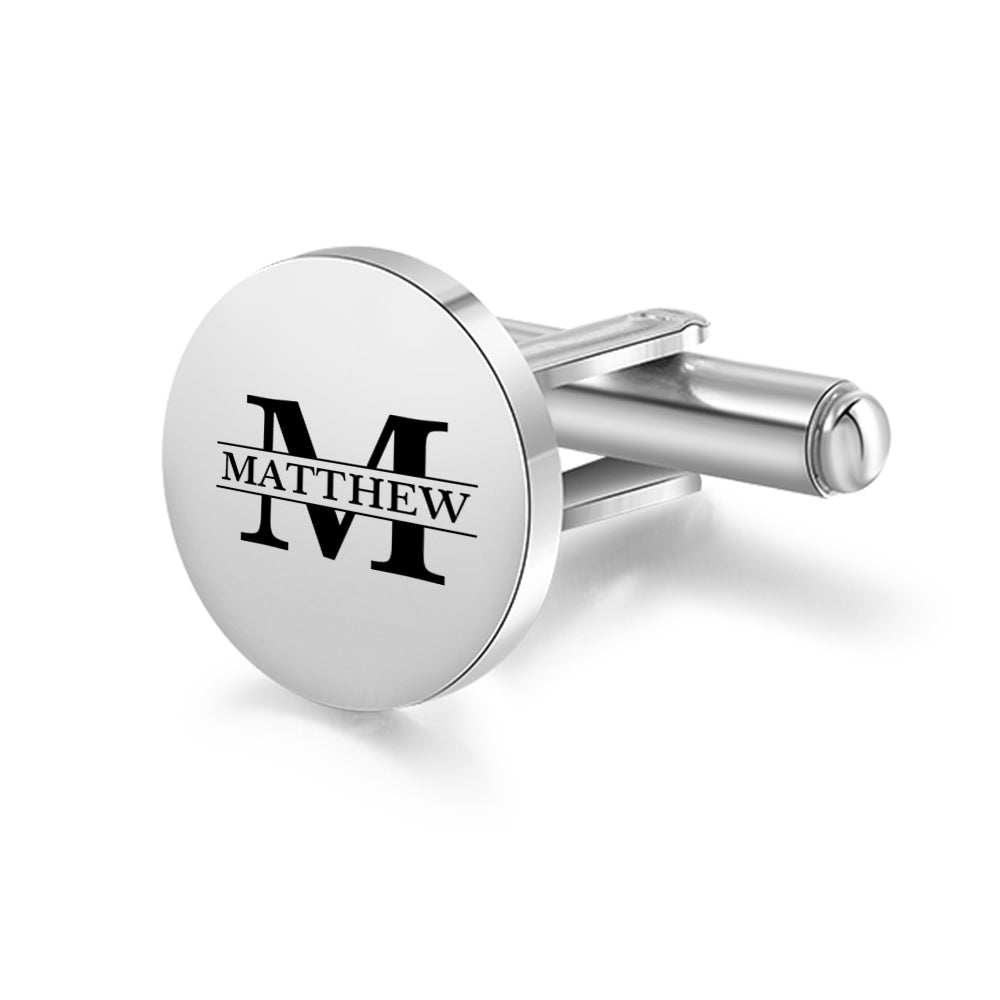 Round stainless steel cufflink with black engraved letter M and name Matthew on reflective surface.