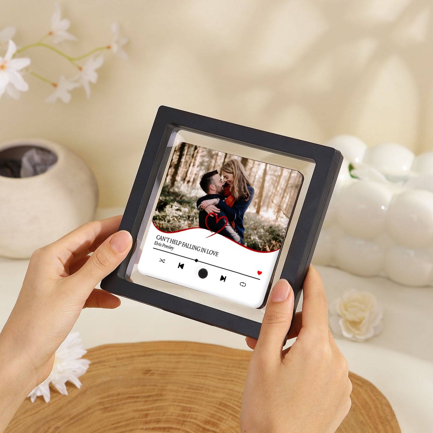 Hands holding a framed photo with a Spotify-style interface, displaying a couple embracing to the song "Can't Help Falling in Love" by Elvis Presley.